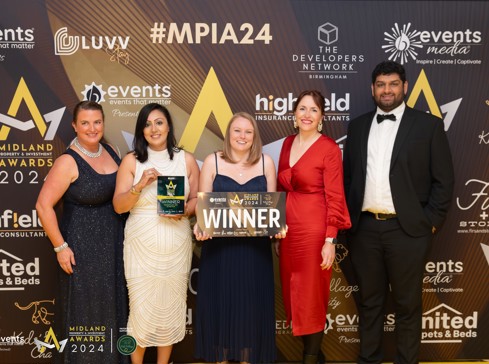 Group of five lawyers dressed up for awards dinner. Standing in front of award signage. Holding winners trophy