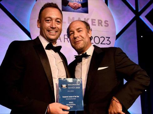 Two men in black tie suits. One is a lawyer holding an award trophy