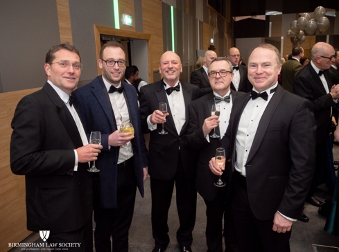 Group of male lawyers wearing black tie suits holding drink glasses